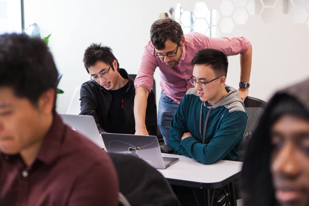 Coding bootcamp instructor helping students on laptops