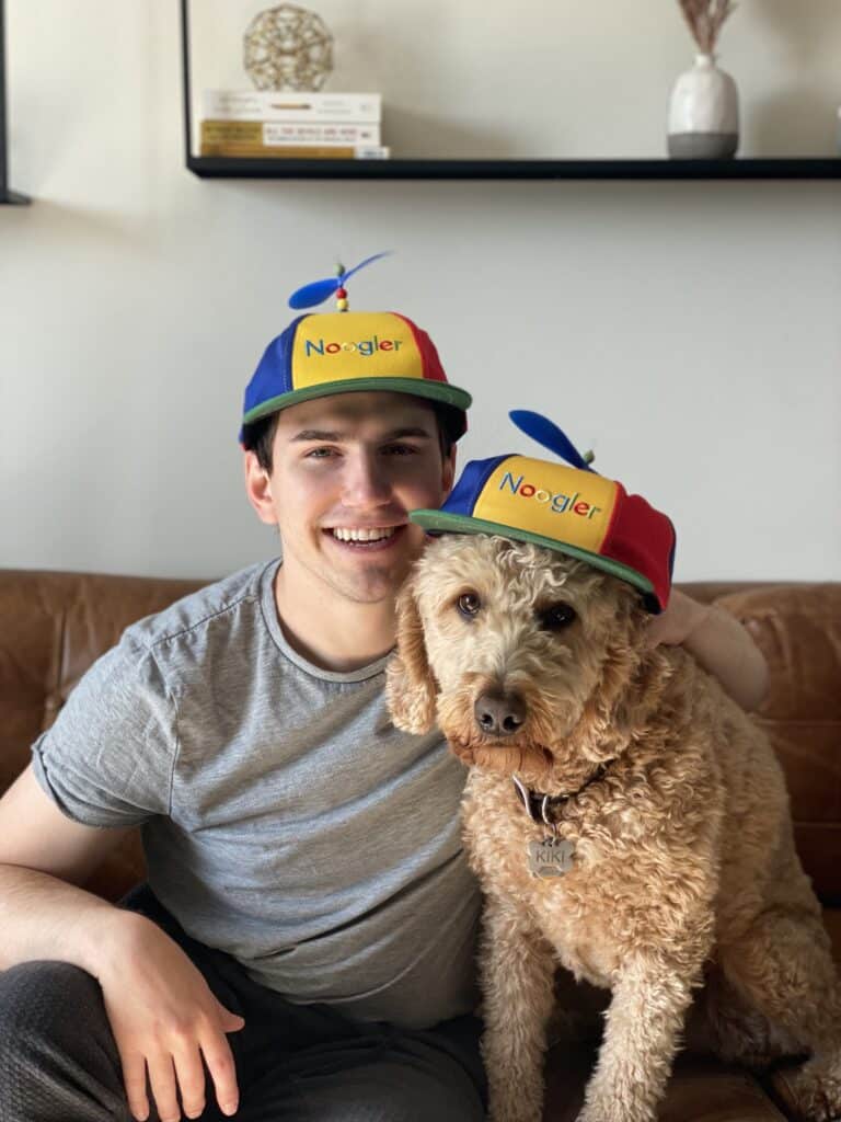 Photo of coding bootcamp graduate with his dog, both wearing Noogler hats from Google